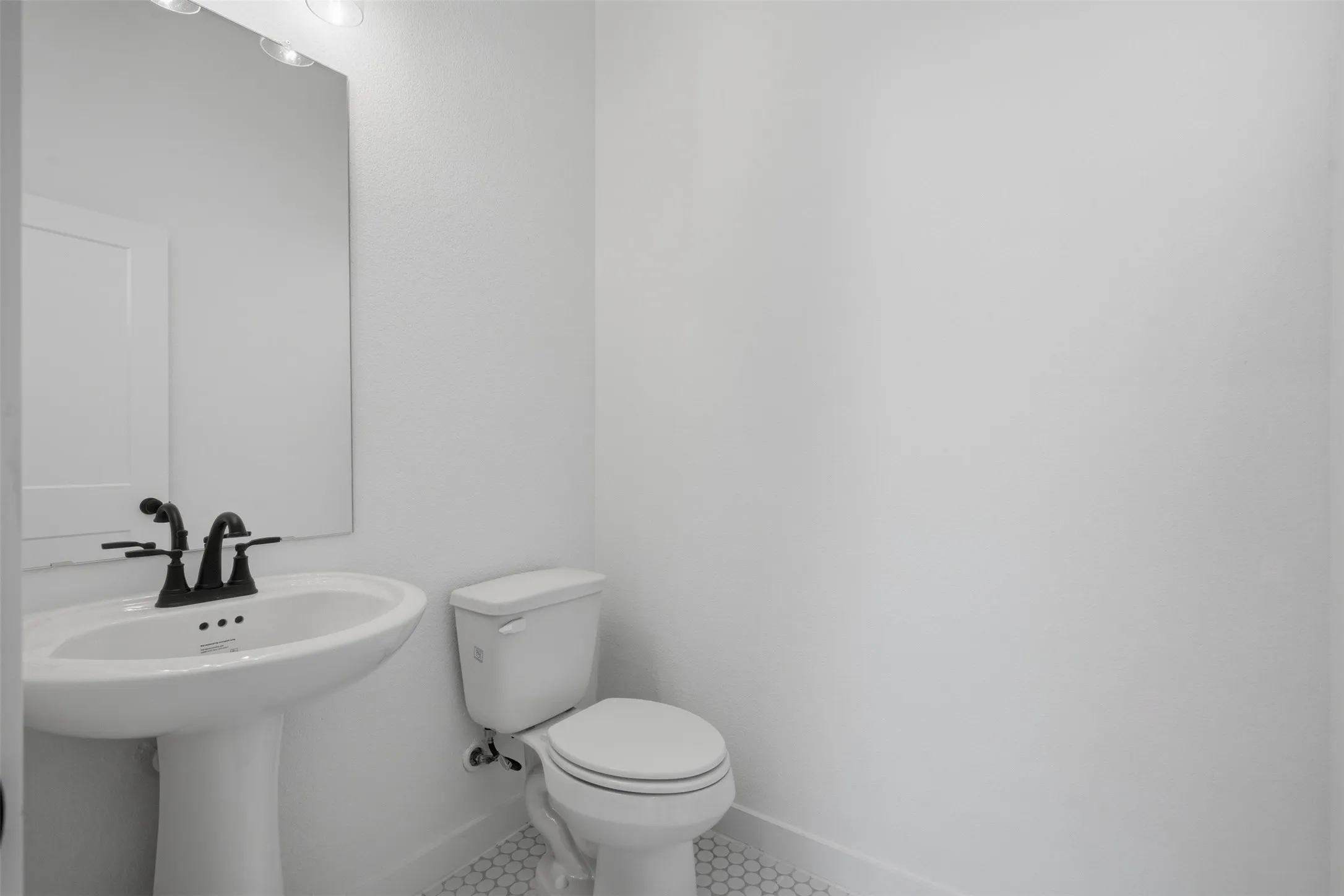 Pedestal sink with a matte black faucet, mirrored vanity, and hexagonal tile flooring