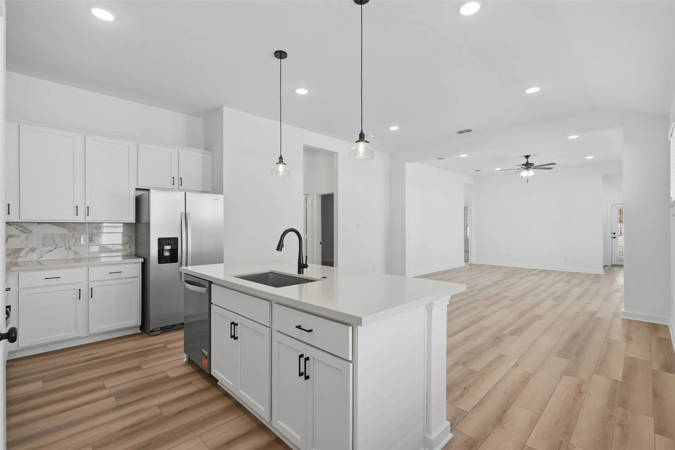 White cabinetry with black hardware, stainless steel appliances, wood-finish flooring, recessed lighting, and an island with pendant lighting