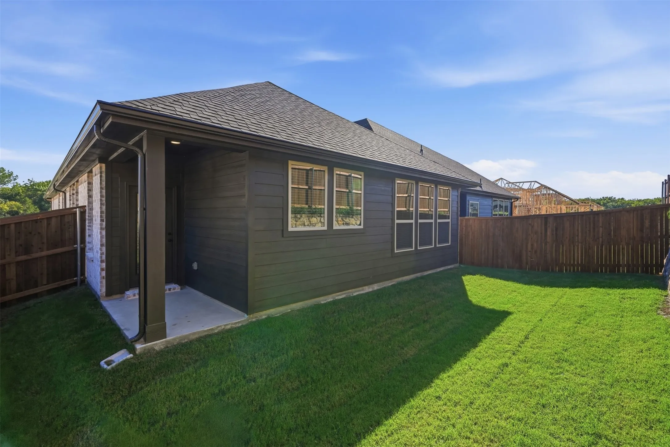 Expansive green lawn with a dark wood privacy fence, featuring a covered patio and dark siding exterior