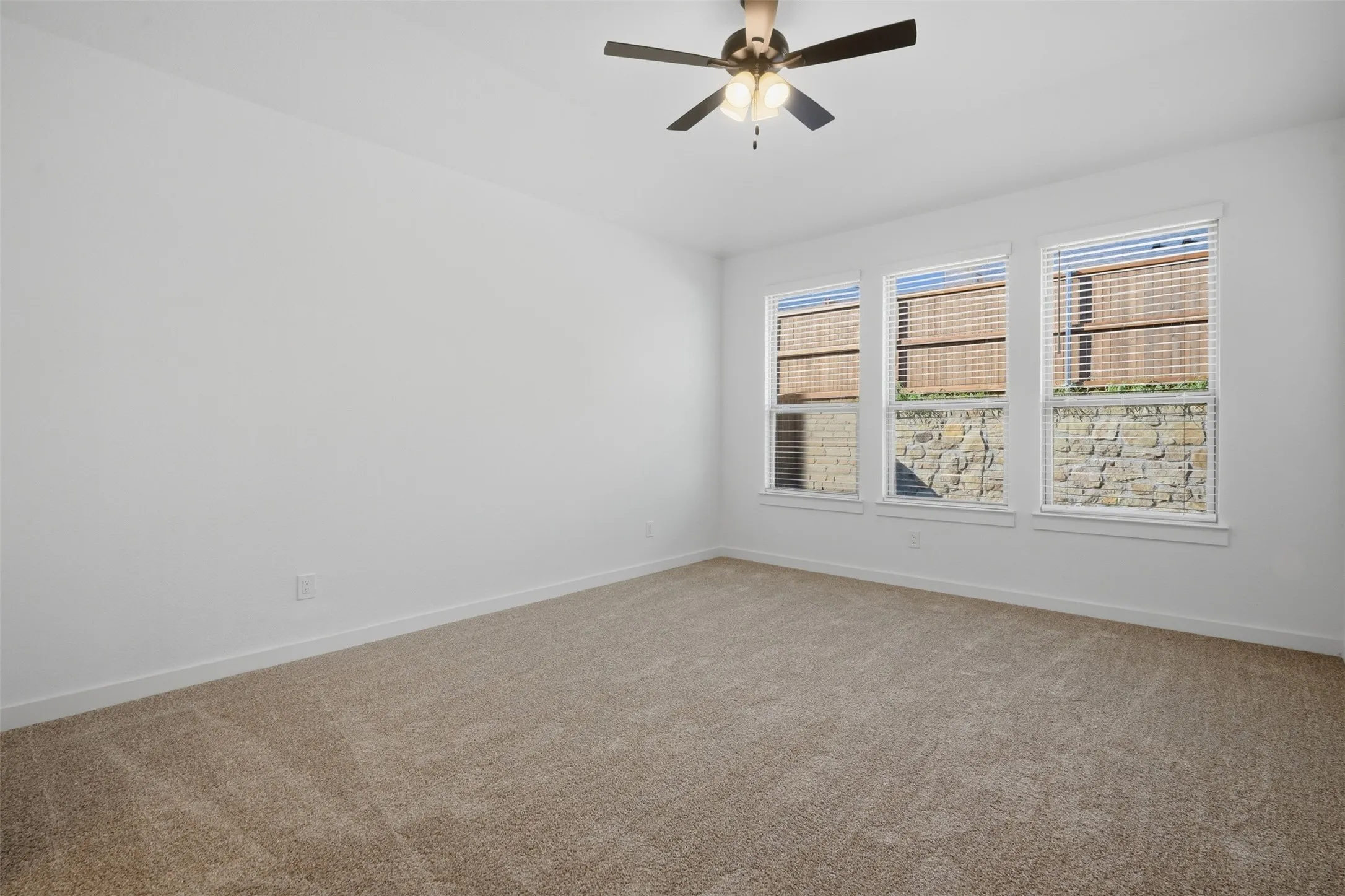 Three large windows with blinds, ceiling fan with integrated lighting, and neutral carpeting
