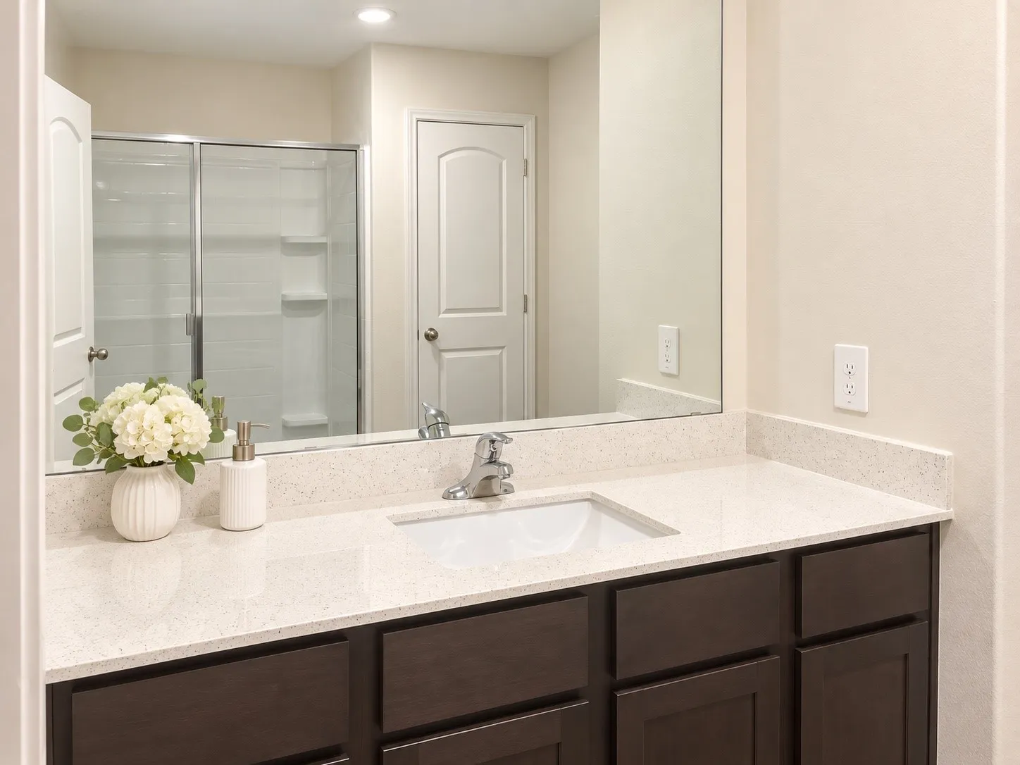 Integrated vanity with white countertop and undermount sink, dark wood-finish cabinetry, and a large wall-mounted mirror