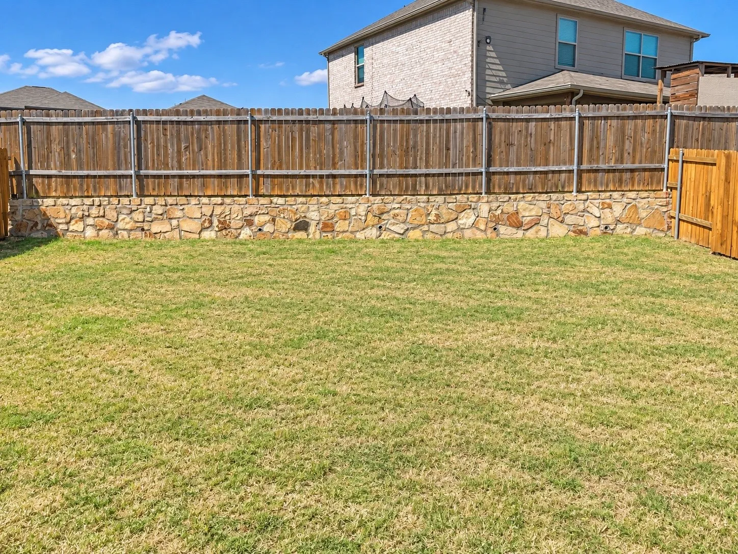 Expansive grass lawn with a stone retaining wall and privacy fencing