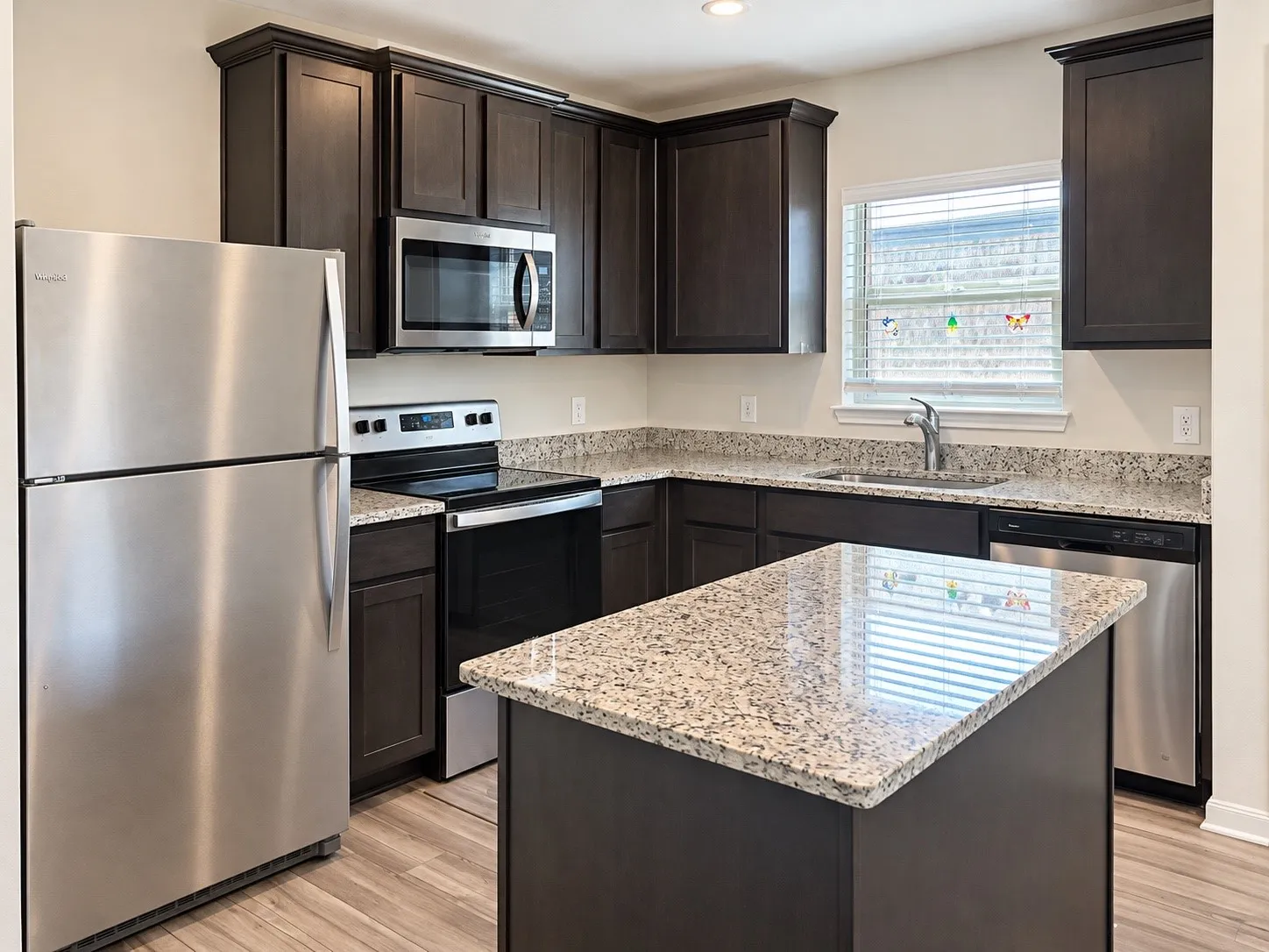 Kitchen featuring dark wood cabinetry, granite countertops, stainless steel appliances, and wood-finish flooring
