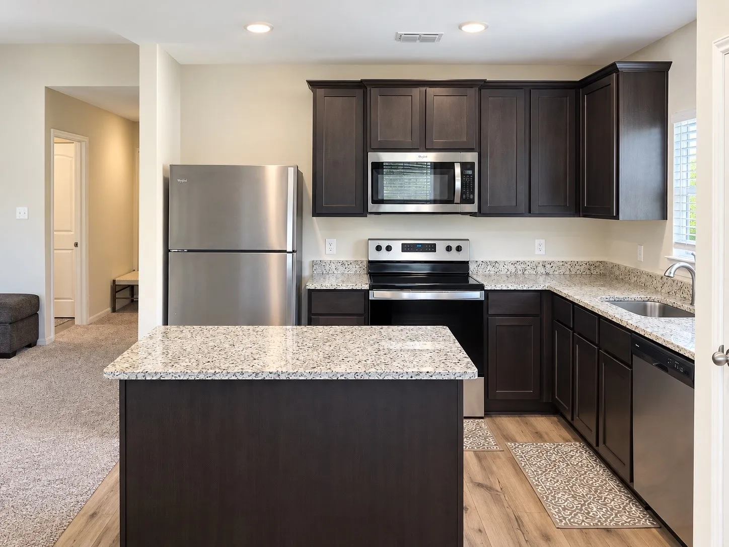 Kitchen featuring dark wood-finish cabinetry, light speckled countertops, stainless steel appliances, and wood-finish flooring