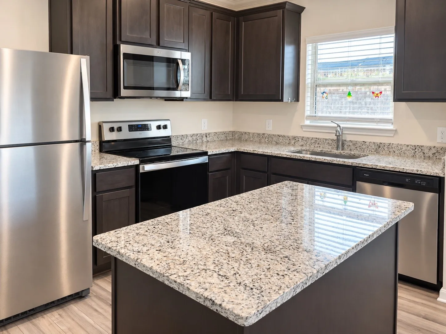 Kitchen featuring dark wood-finish cabinetry, light-toned granite countertops, and stainless steel appliances