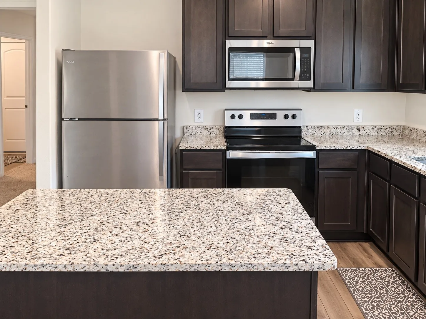 Kitchen featuring wood-finish flooring, dark wood cabinetry, granite countertops, stainless steel appliances, and a built-in microwave