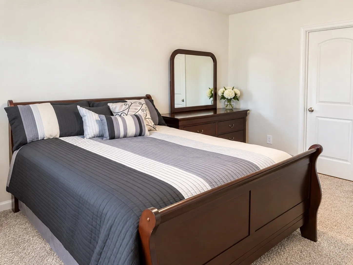 Plush carpet flooring, neutral painted walls, white two-panel interior door, and dark wood-finish furniture