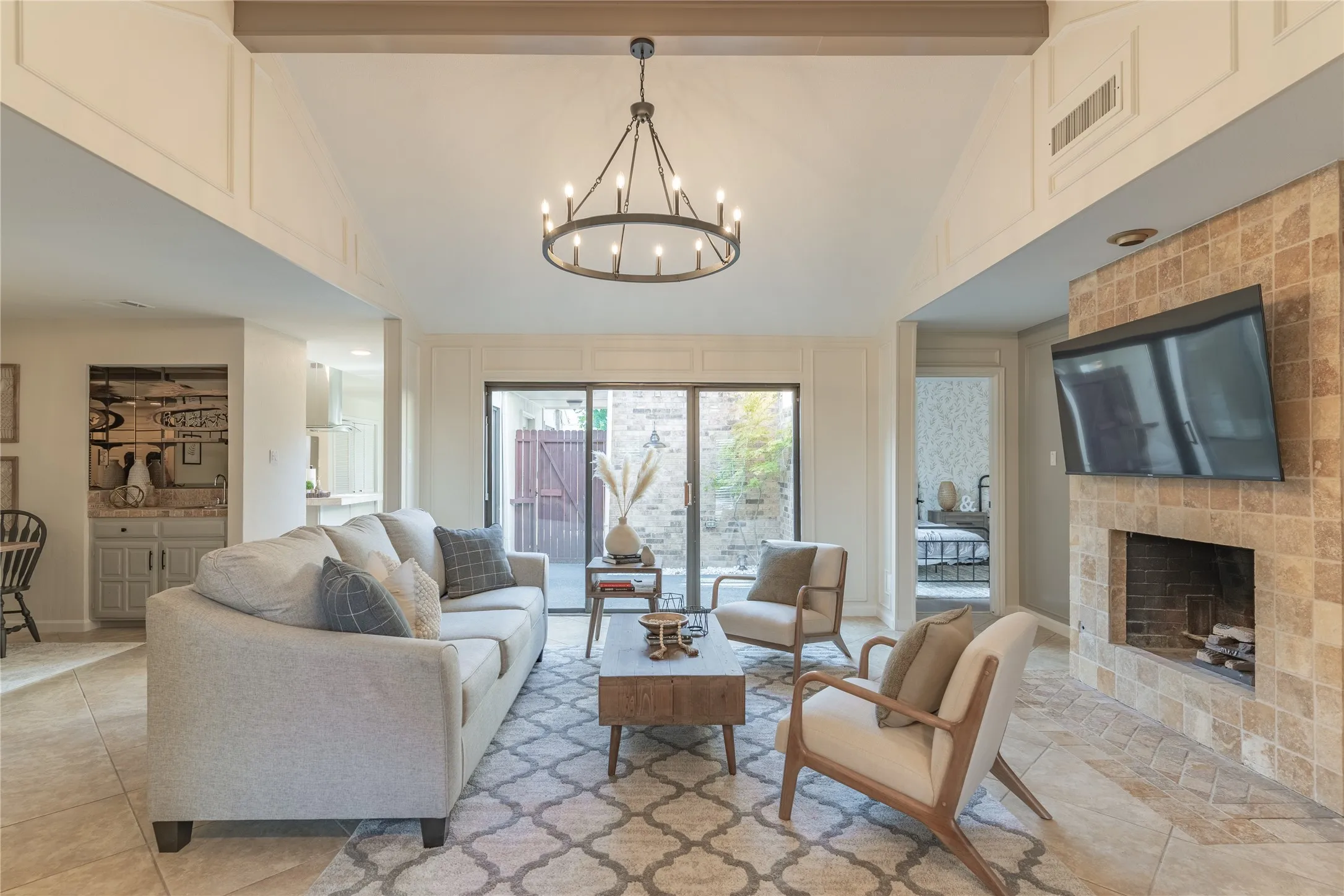 Vaulted ceiling with exposed beam, tile flooring, stone-tiled fireplace, built-in wet bar, and sliding glass door