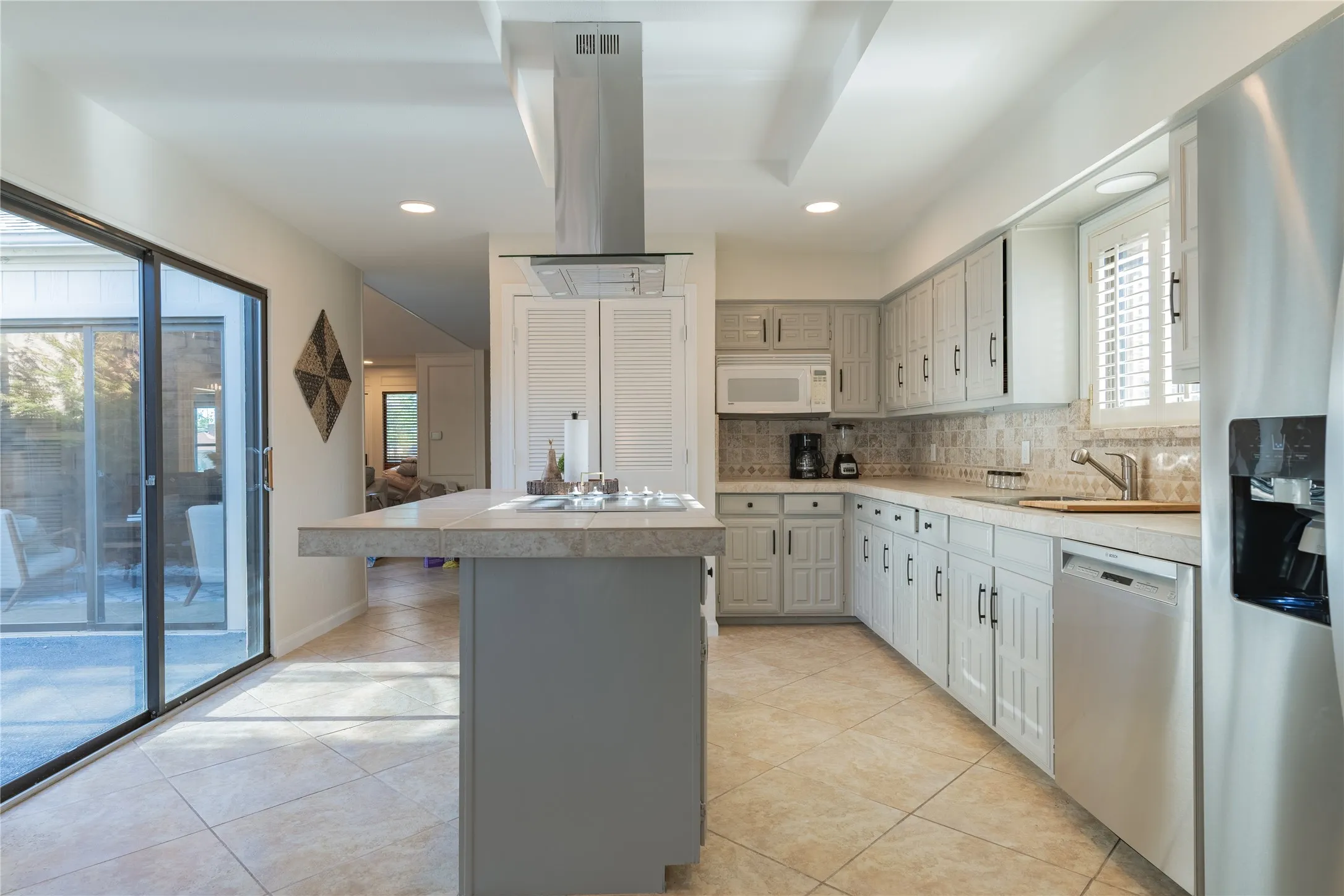 Kitchen featuring neutral tile flooring, light-toned cabinetry, light countertops, stainless steel appliances, and a sliding glass door