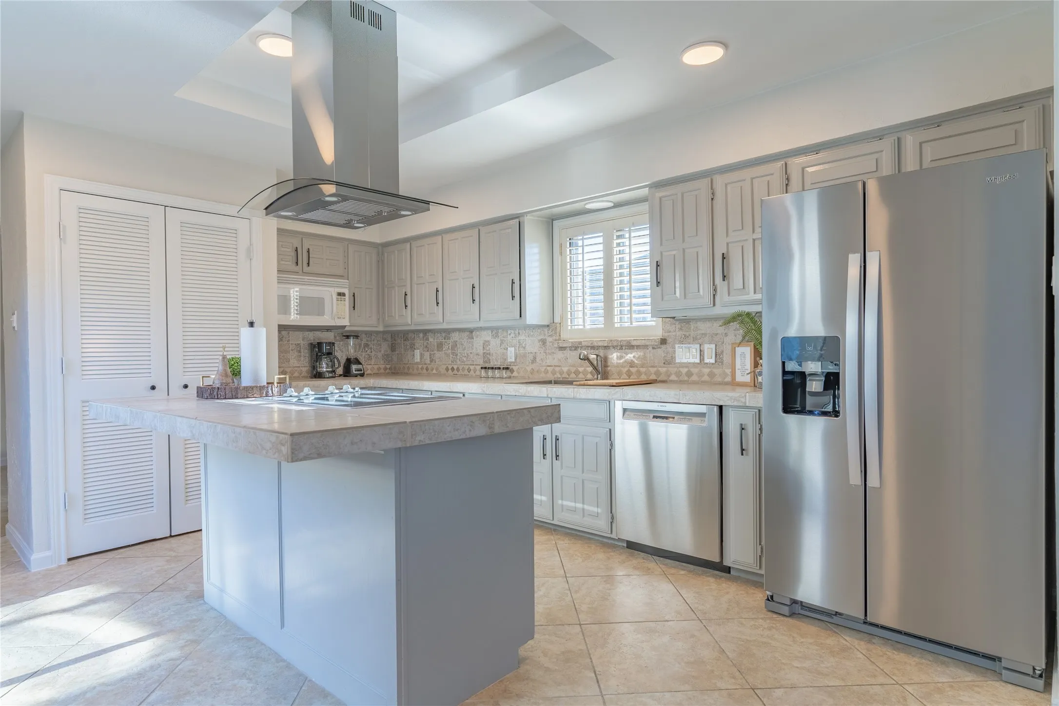 Kitchen featuring an island with cooktop, stainless steel appliances, white cabinetry, decorative backsplash, and tiled flooring