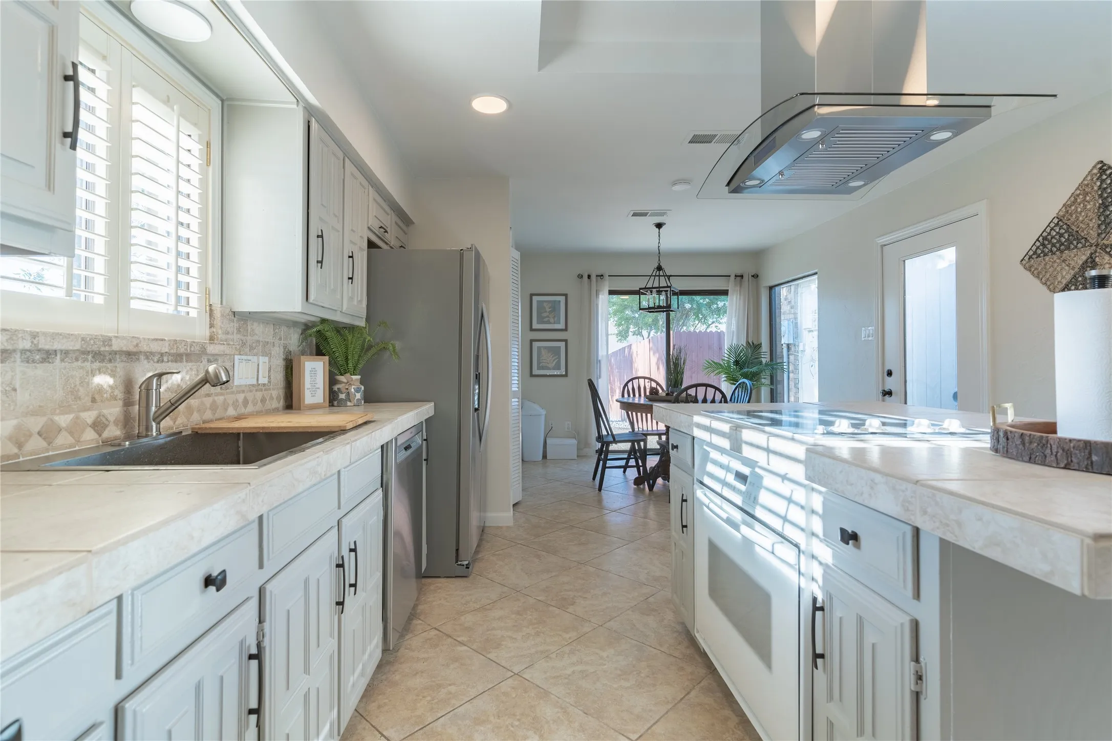 Recessed lighting, stainless steel appliances, tile flooring, glass-front cabinetry, and a ceiling-mounted range hood