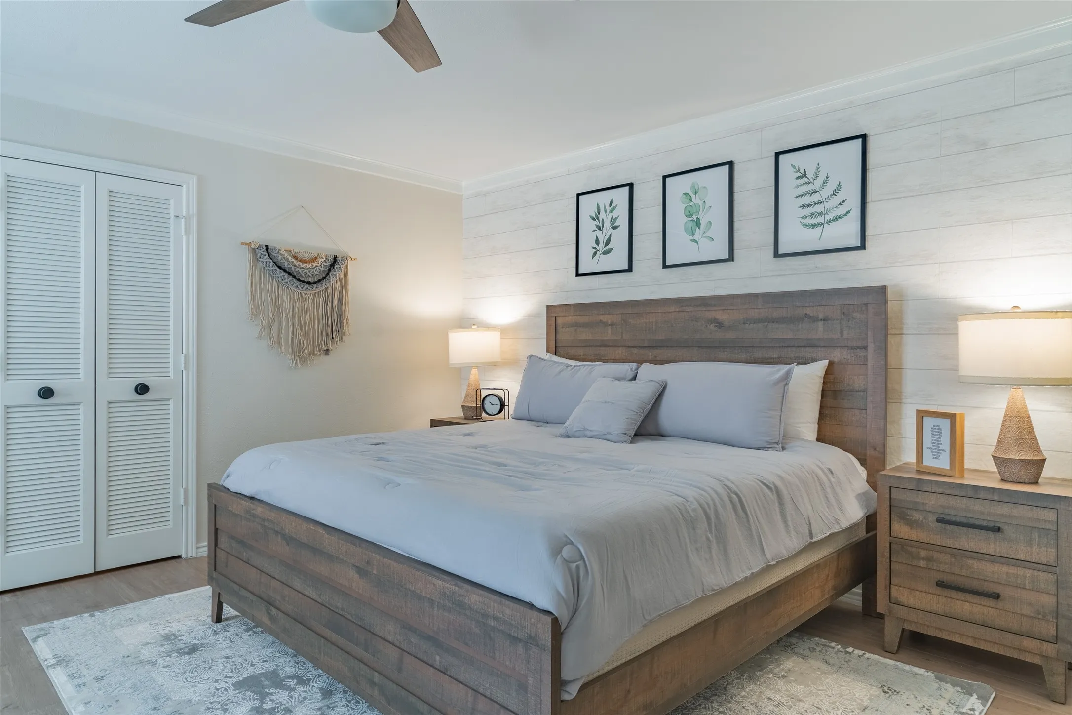 Wood-finish flooring, white shiplap accent wall, louvered bi-fold closet doors, ceiling fan with integrated lighting, and crown molding
