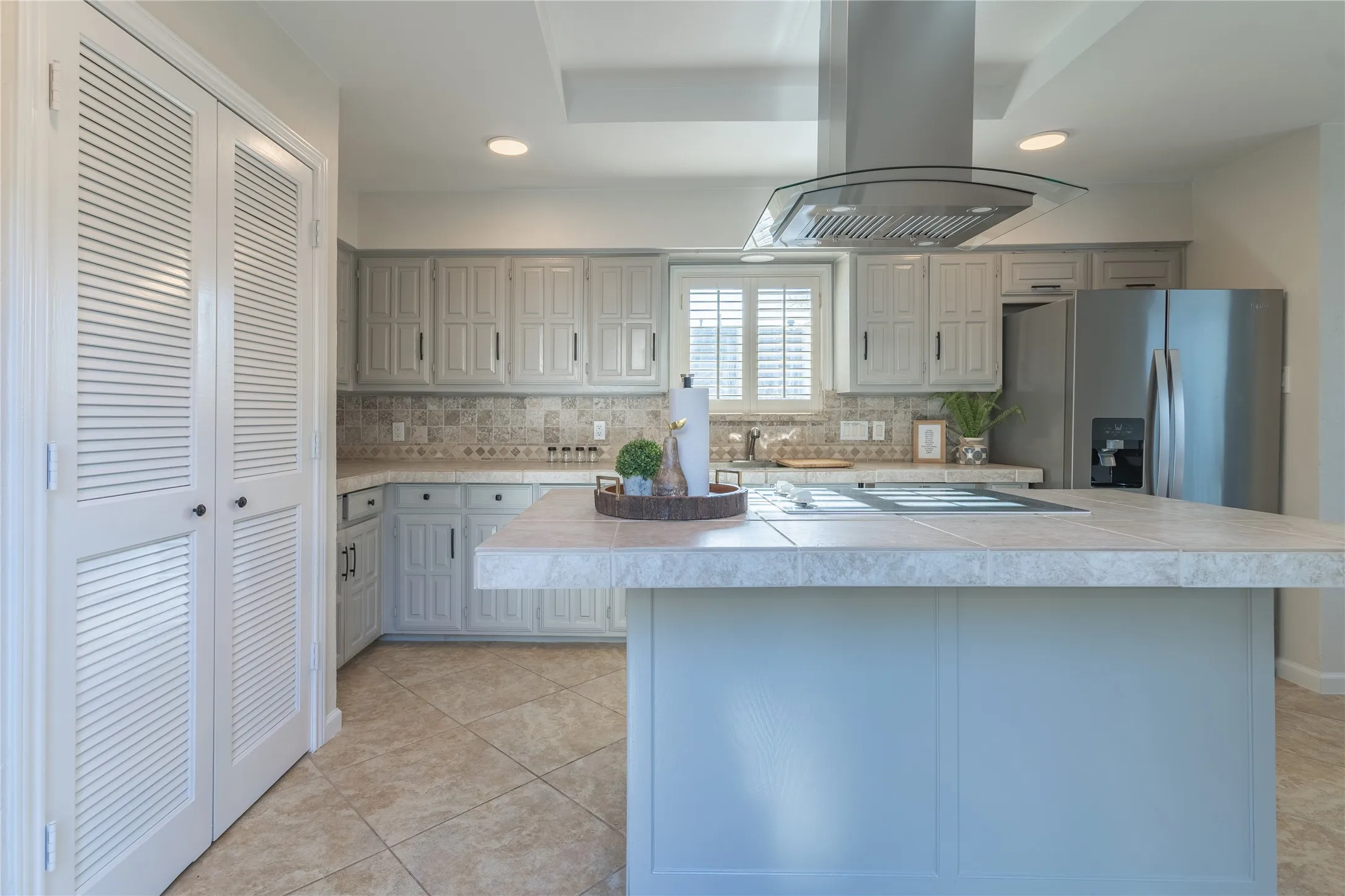 Contemporary kitchen featuring a stainless steel range hood, tile flooring, recessed lighting, and louvered bi-fold doors