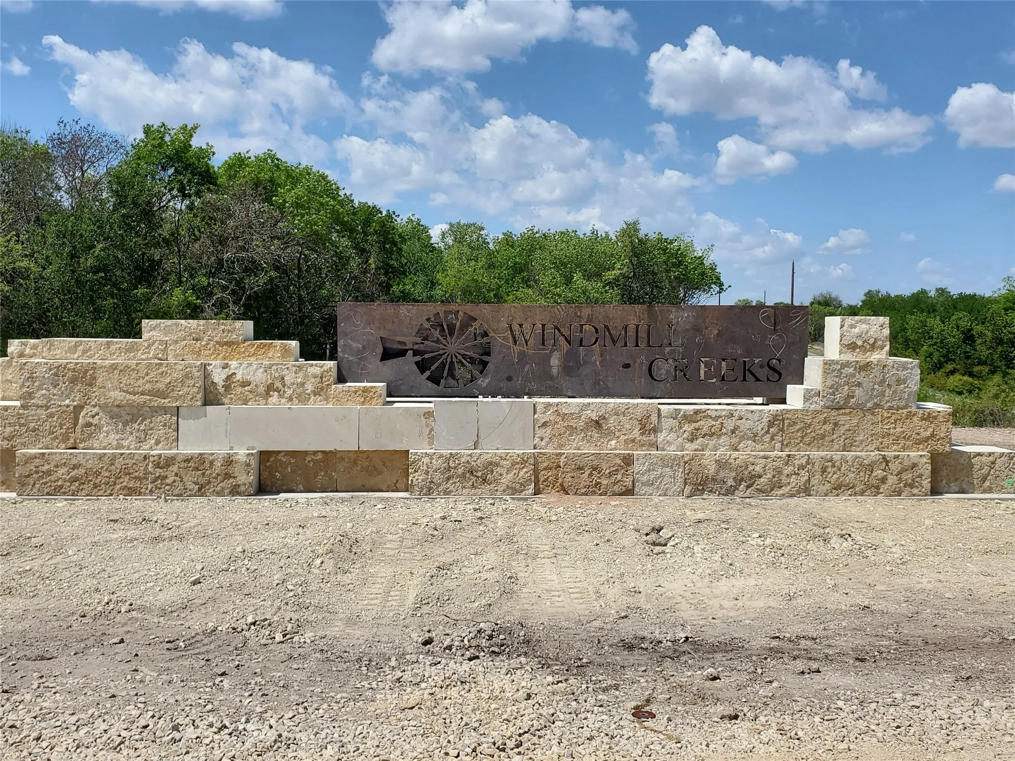 Tiered stone retaining wall with a custom metal sign featuring a windmill motif and community name