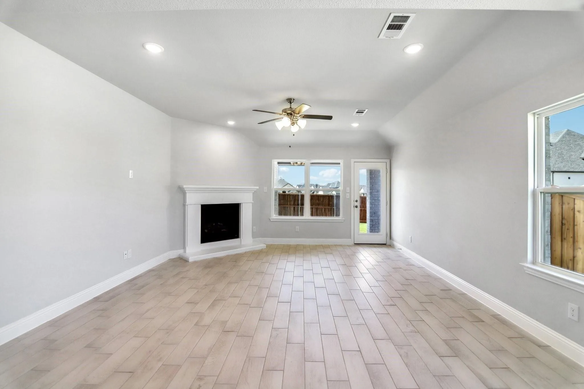 Spacious room featuring wood-finish flooring, a built-in fireplace with a white mantel, recessed lighting, a ceiling fan, and multiple windows