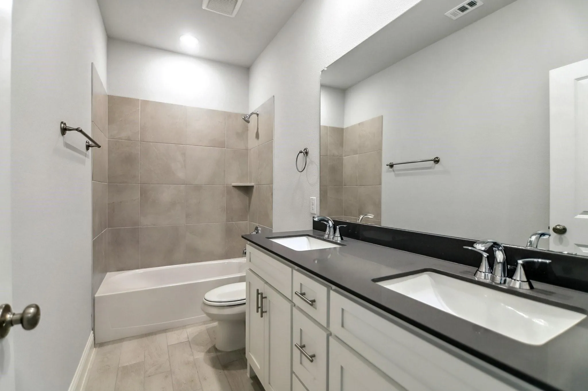 Dual vanity with undermount sinks and dark countertops, wood-finish flooring, tiled bath and shower combination, and integrated lighting