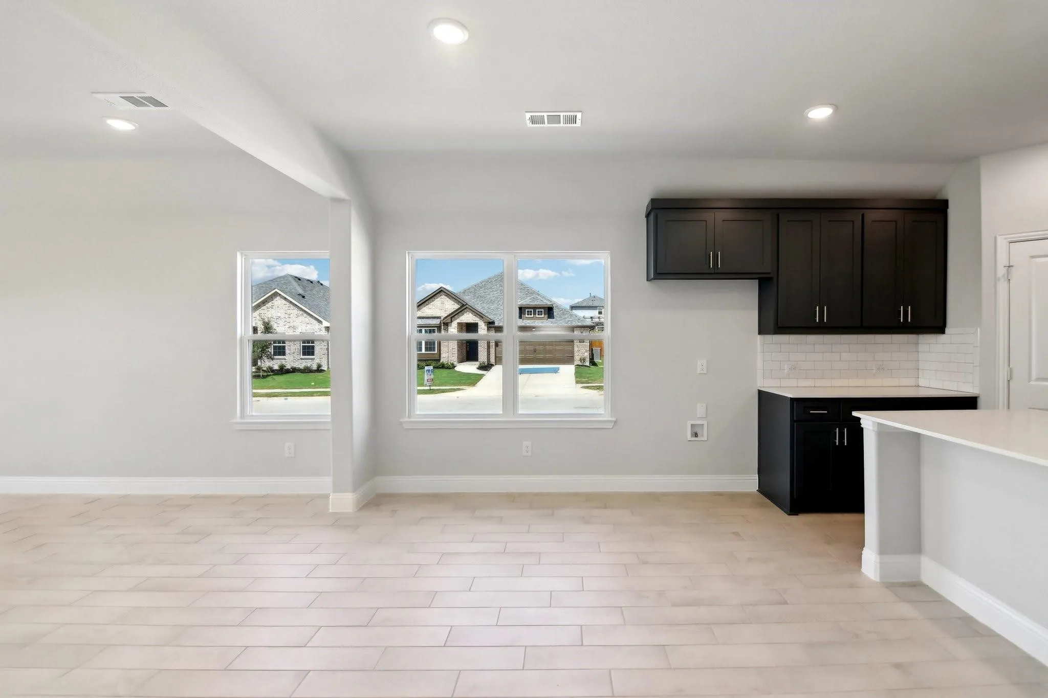 Recessed lighting, wood-finish flooring, white walls, dark cabinetry, and a white subway tile backsplash
