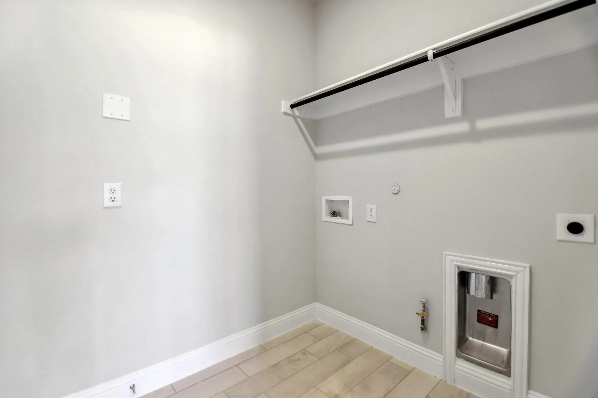 Wood-finish flooring with white baseboards, a built-in shelf and rod, and hookups for appliances
