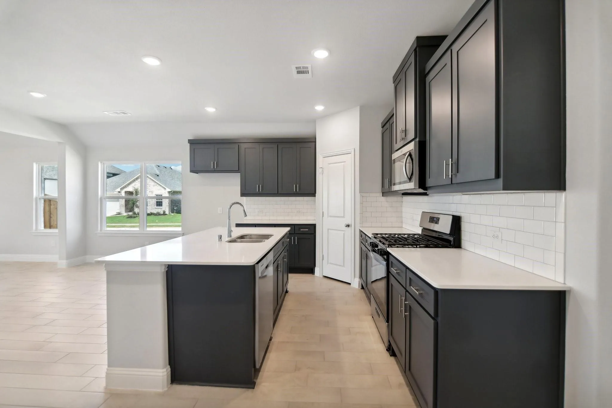 Kitchen featuring an island with an undermount sink, stainless steel appliances, dark cabinetry, light countertops, and a subway tile backsplash