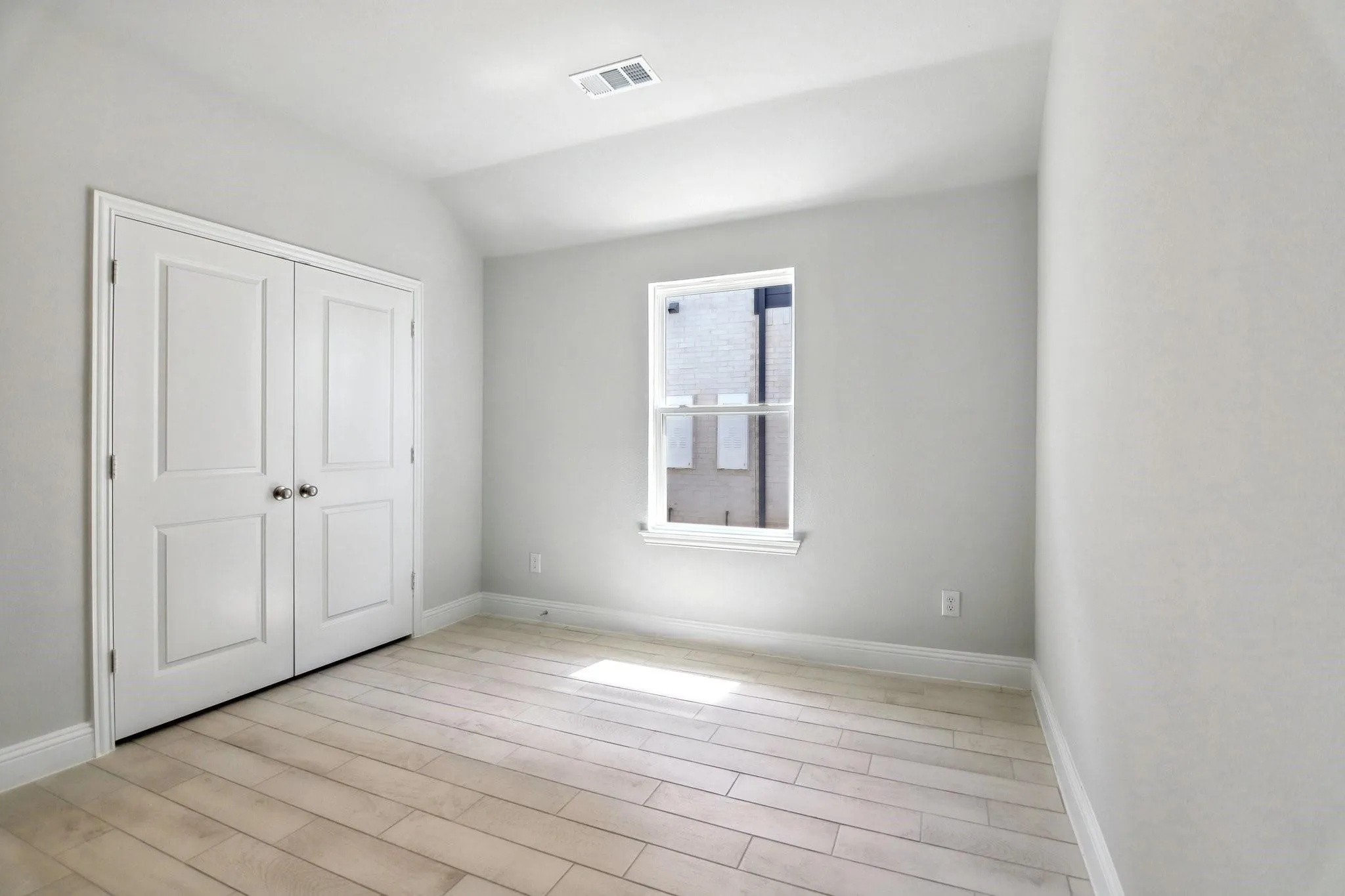 Light-toned wood-finish flooring, crisp white walls, single window, and double panel doors