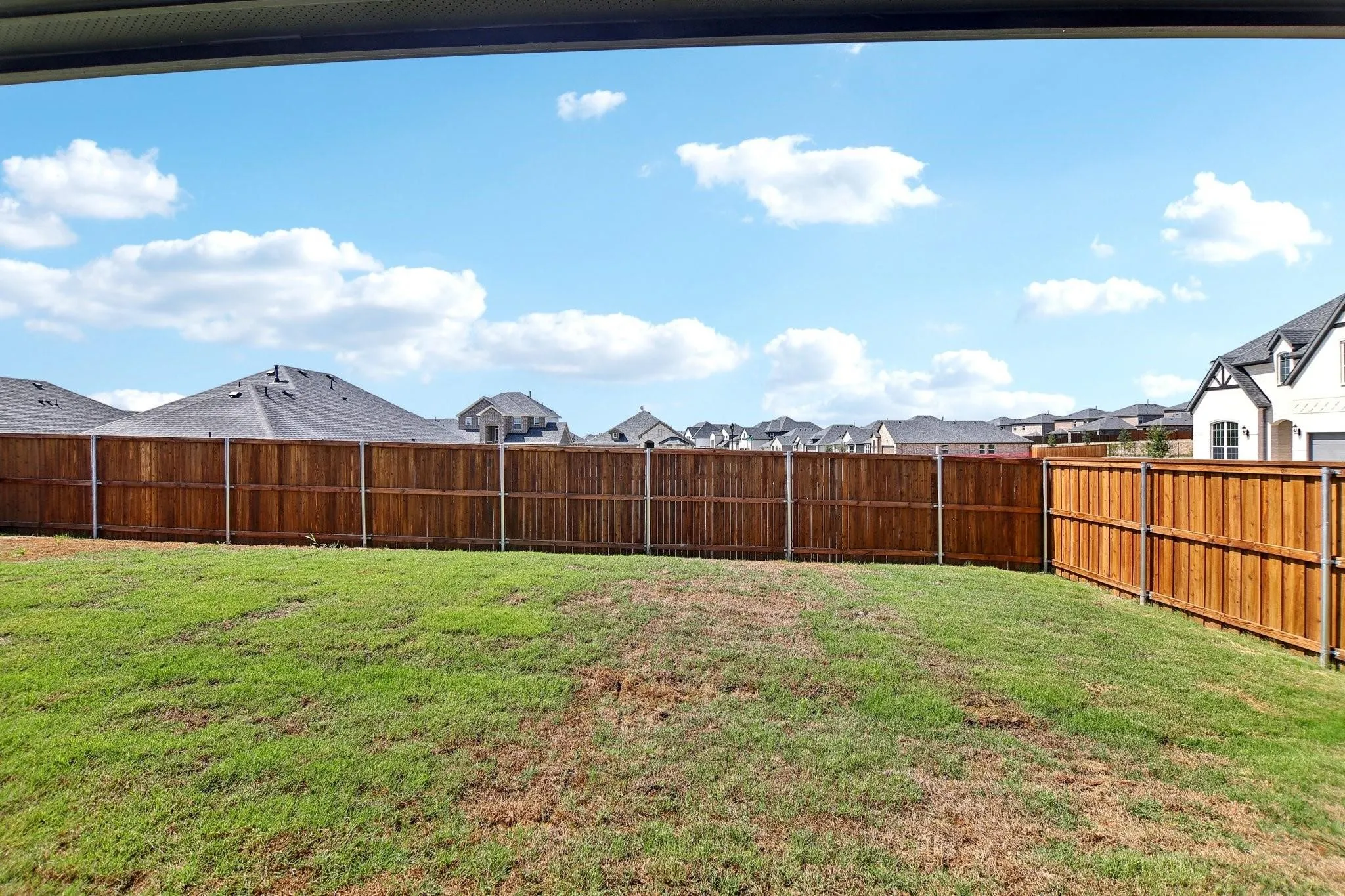 Expansive outdoor space featuring a wood fence, green lawn, and residential roofs in the background