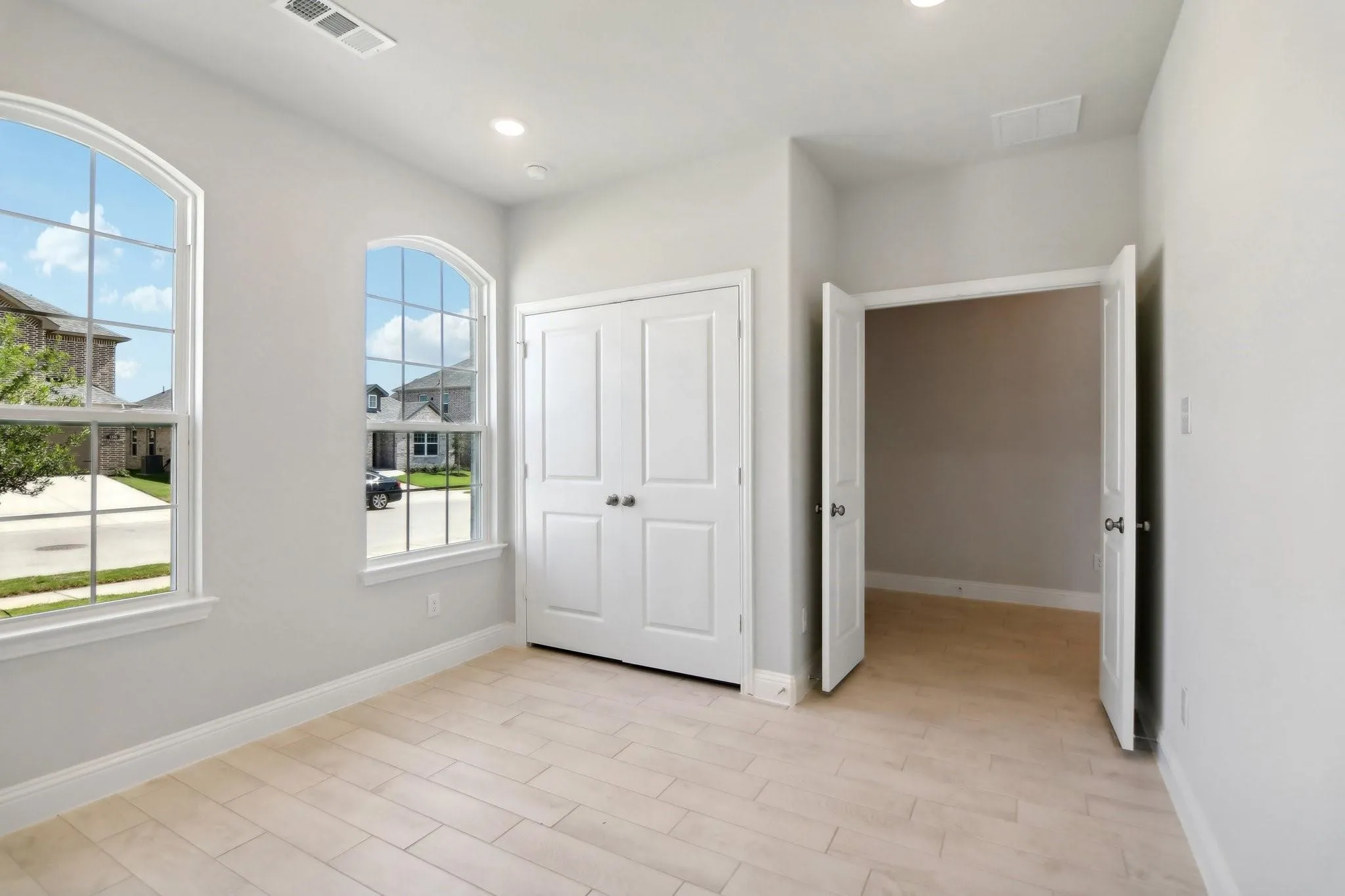 Light-toned wood-finish flooring, two arched windows with gridded panes, built-in double-door closet, and recessed ceiling lighting