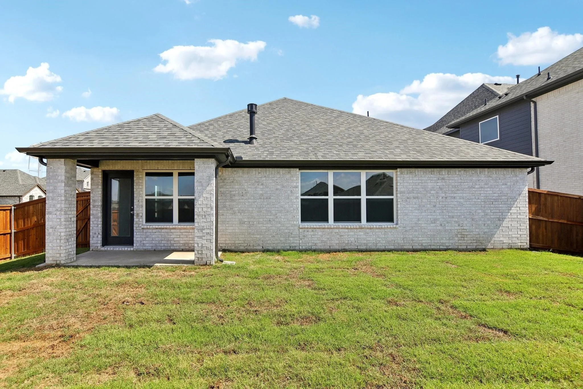Expansive backyard featuring a covered patio, brick exterior, multiple windows, and a wood privacy fence
