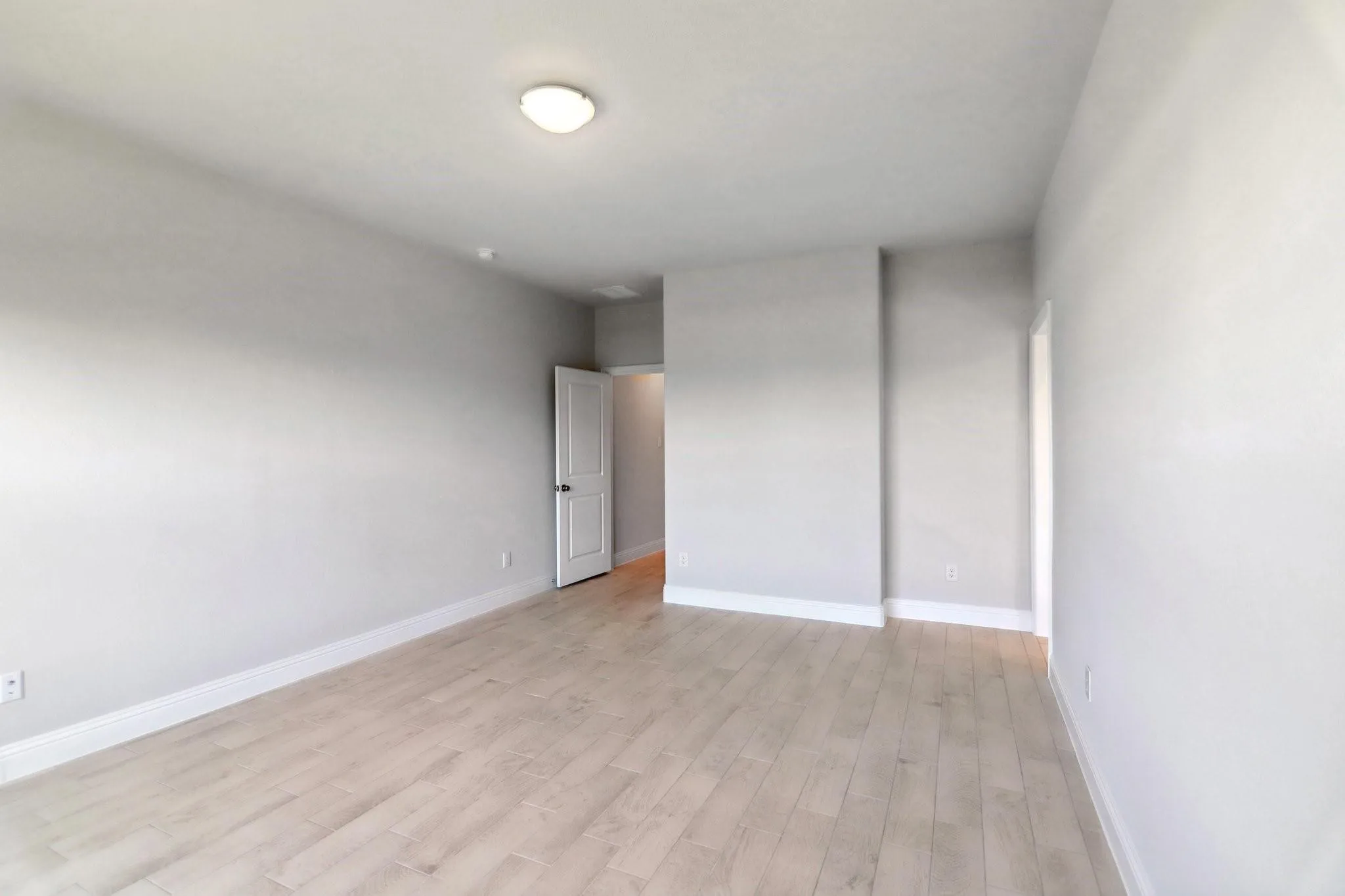 Spacious room featuring light wood-finish flooring, neutral wall paint, and recessed lighting