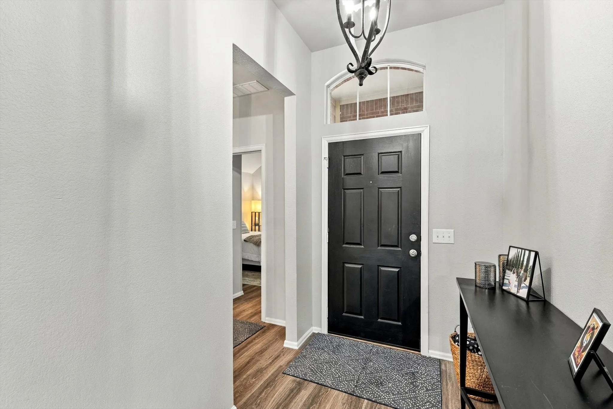 Black paneled entry door with an arched transom window and overhead chandelier