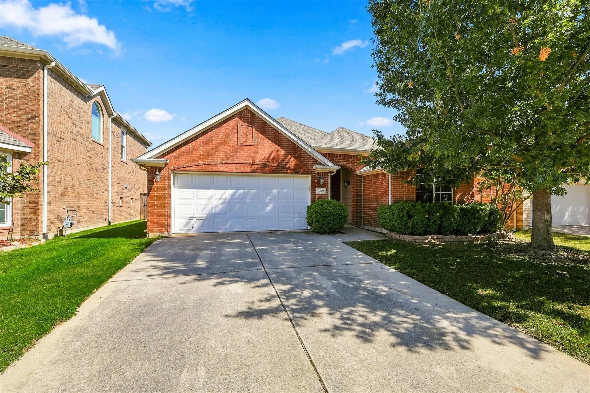 Brick facade home with an attached garage, concrete driveway, and mature landscaping