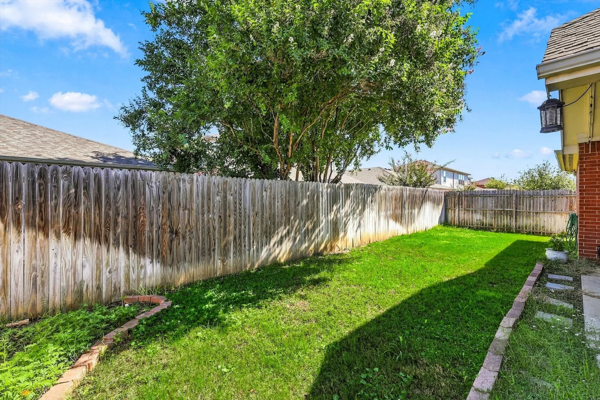 Expansive backyard featuring a manicured lawn, mature trees, and a durable wood privacy fence