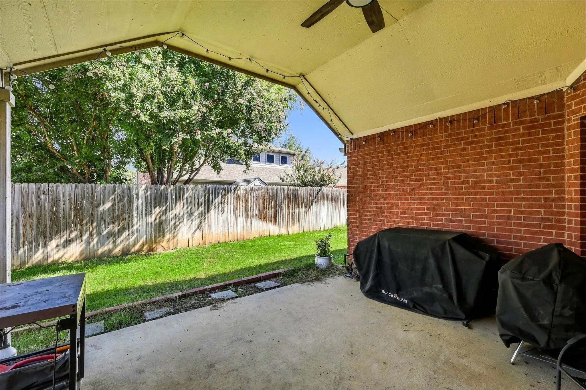 Covered concrete patio with a ceiling fan, brick exterior wall, and string lights