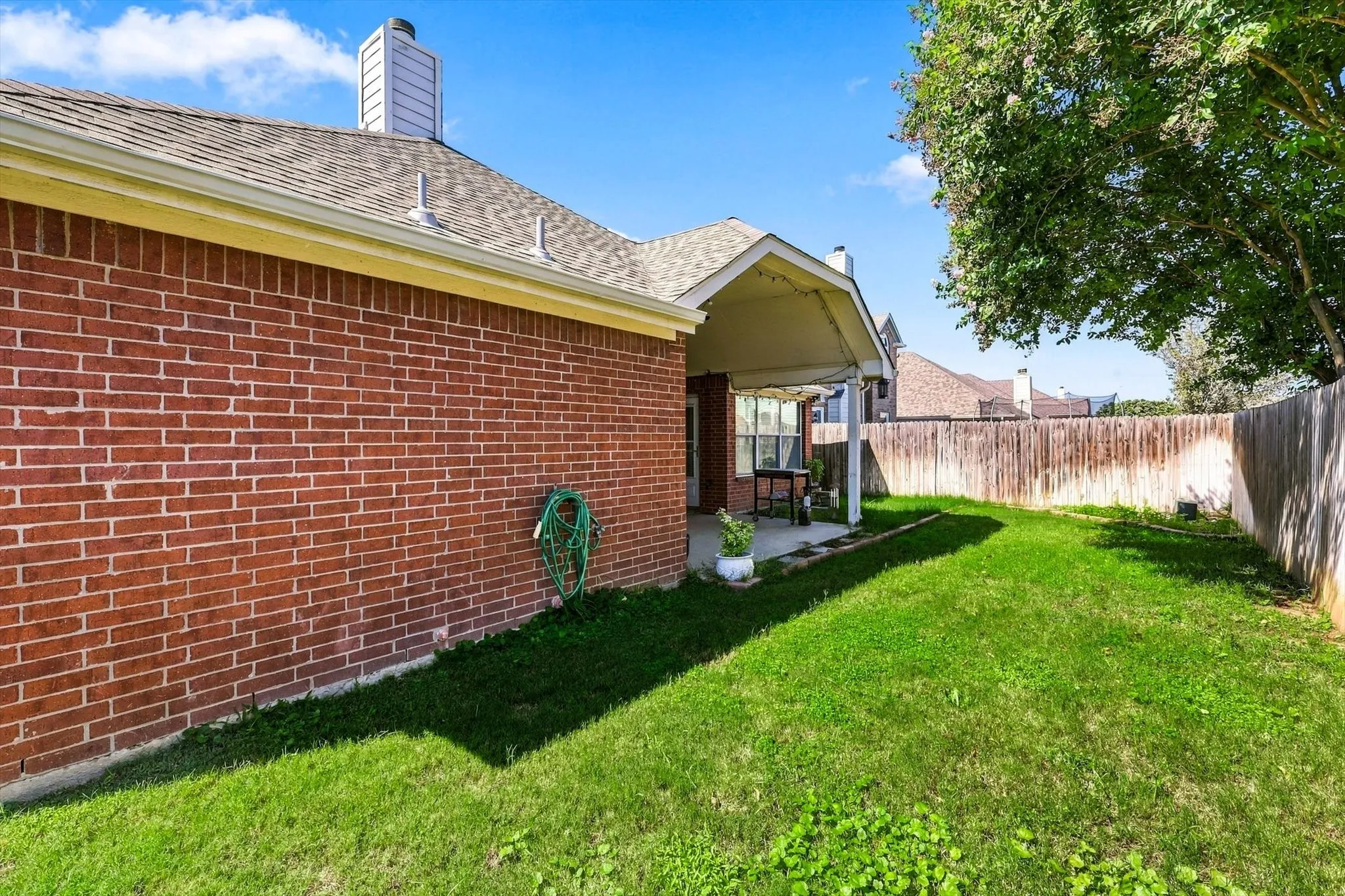 Expansive backyard featuring a manicured lawn, brick exterior, covered patio, and wood privacy fencing