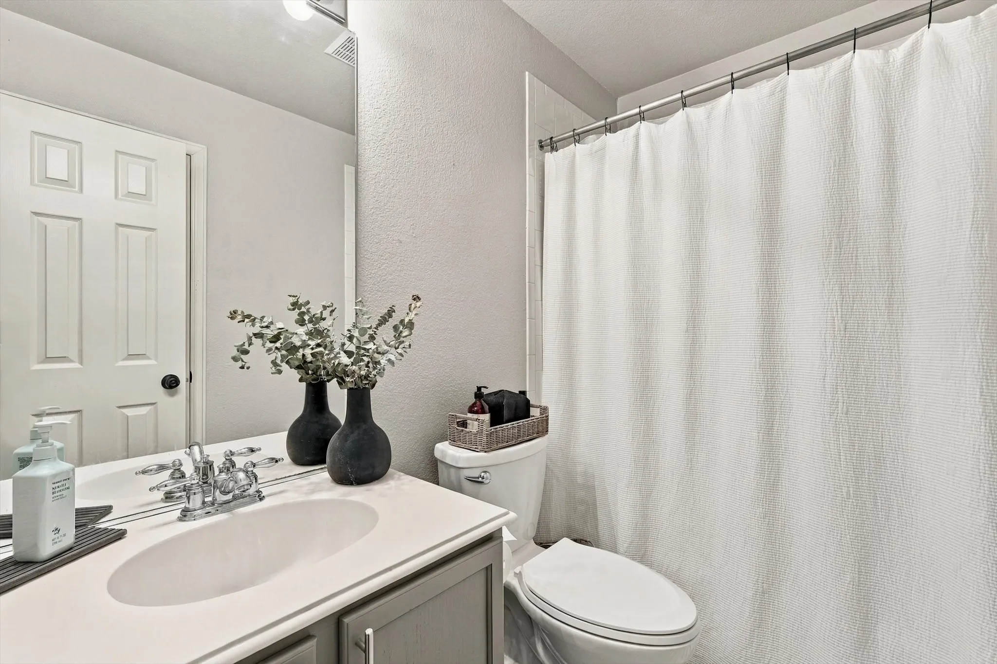 Vanity with a white countertop and oval sink, chrome faucet, and gray cabinetry