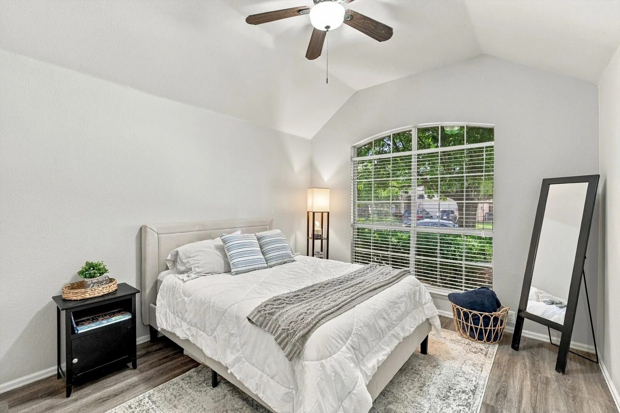 Vaulted ceiling with a ceiling fan, arched window with horizontal blinds, wood-finish flooring, and light-toned walls