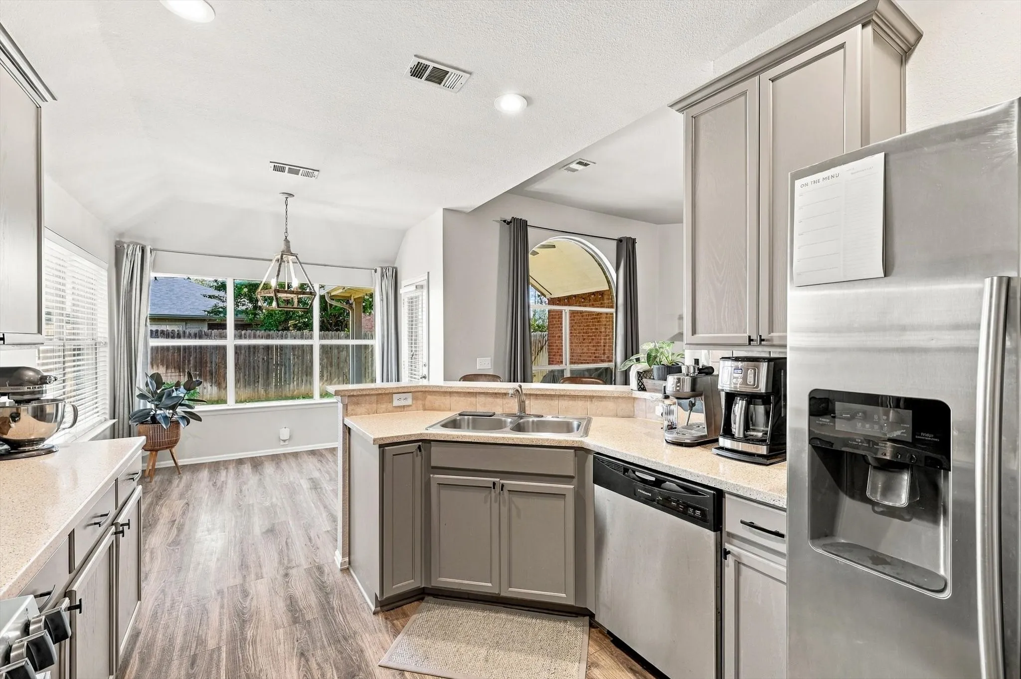 Kitchen featuring recessed lighting, a vaulted ceiling, wood-finish flooring, a stainless steel refrigerator, and ample cabinetry
