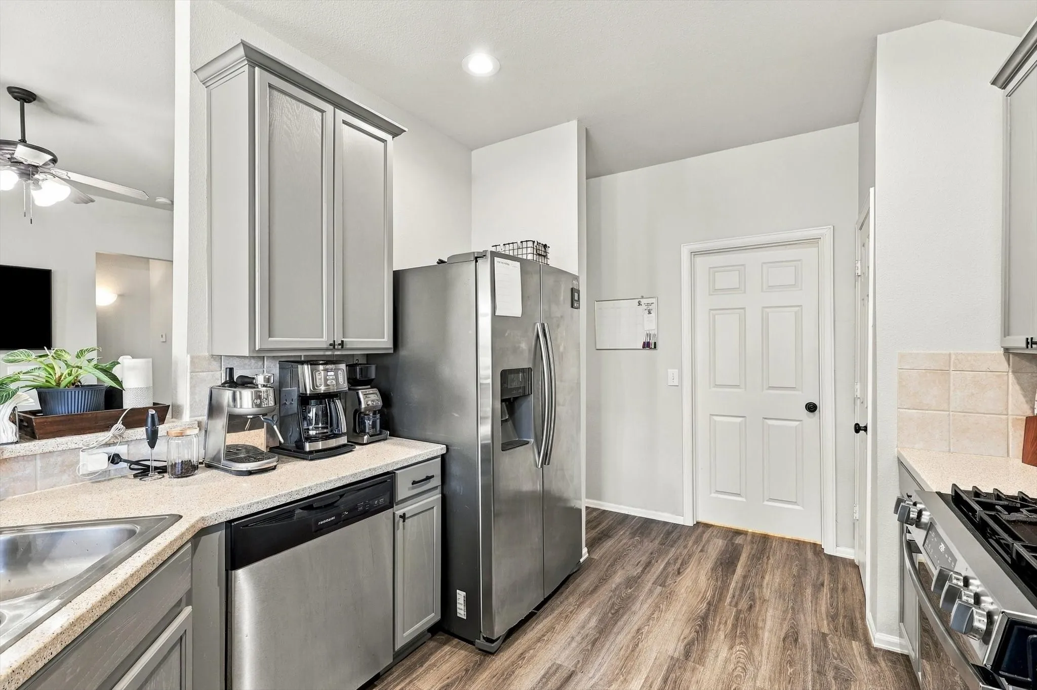 Stainless steel appliances, wood-finish flooring, light grey cabinetry, tile backsplash, and solid surface countertops