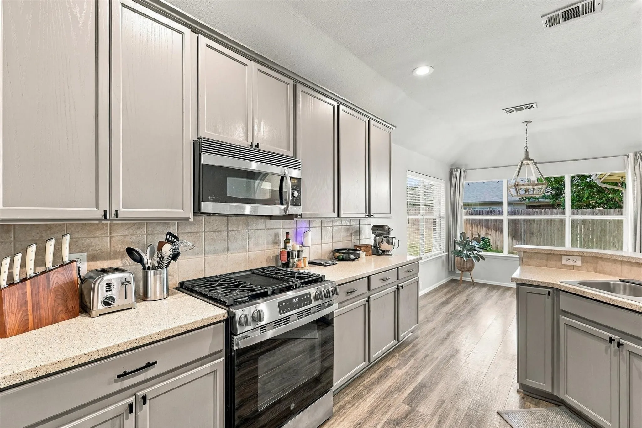 Kitchen featuring light gray cabinetry, light speckled countertops, and a full tile backsplash