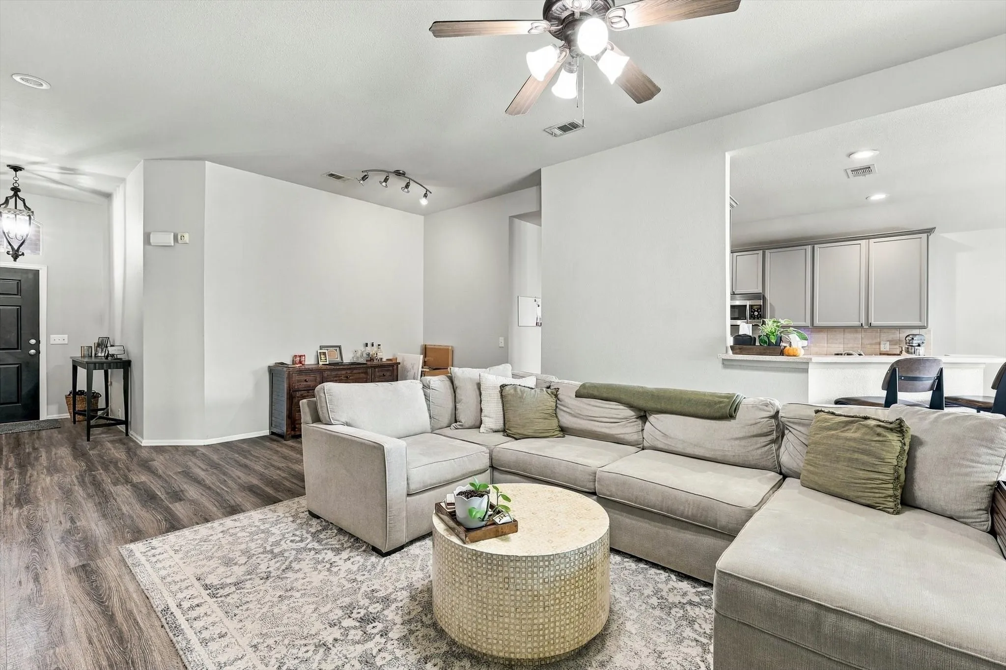 Wood-finish flooring throughout, ceiling fan with integrated lighting, track lighting fixture, and a kitchen pass-through