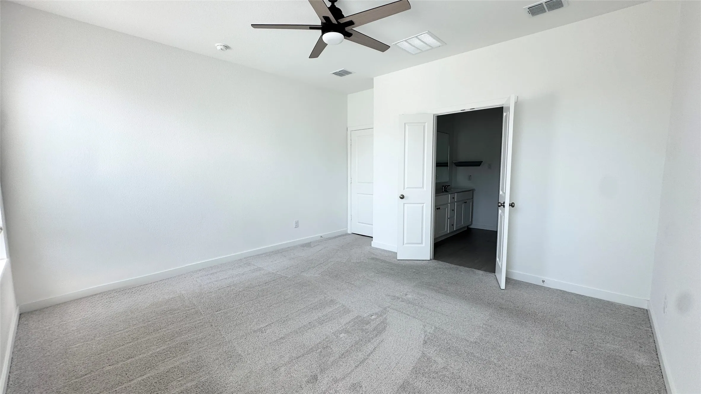 Spacious room featuring neutral carpeting, white walls, and a ceiling fan