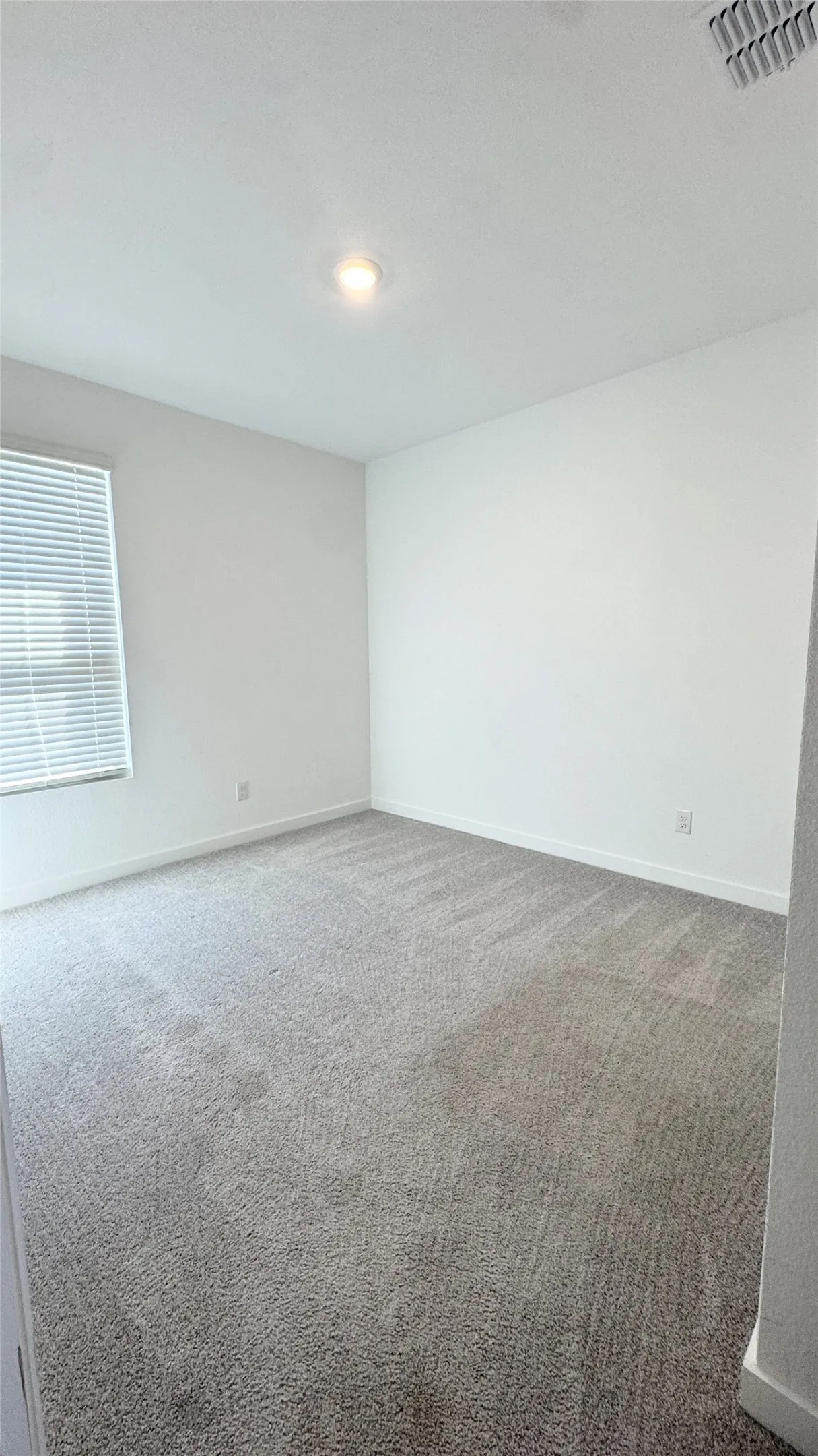 Plush gray carpeting, white walls, recessed lighting, and a window with horizontal blinds