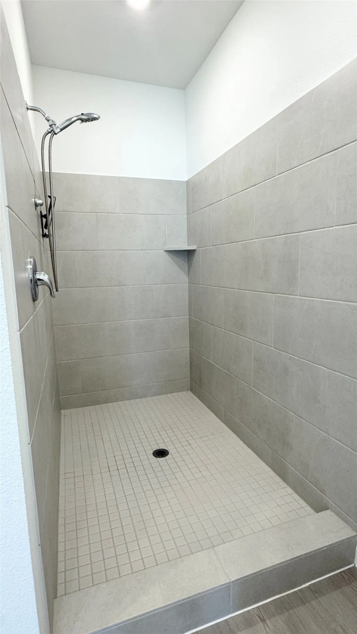Walk-in shower featuring light grey wall tiles, a mosaic tile floor, and a built-in corner shelf