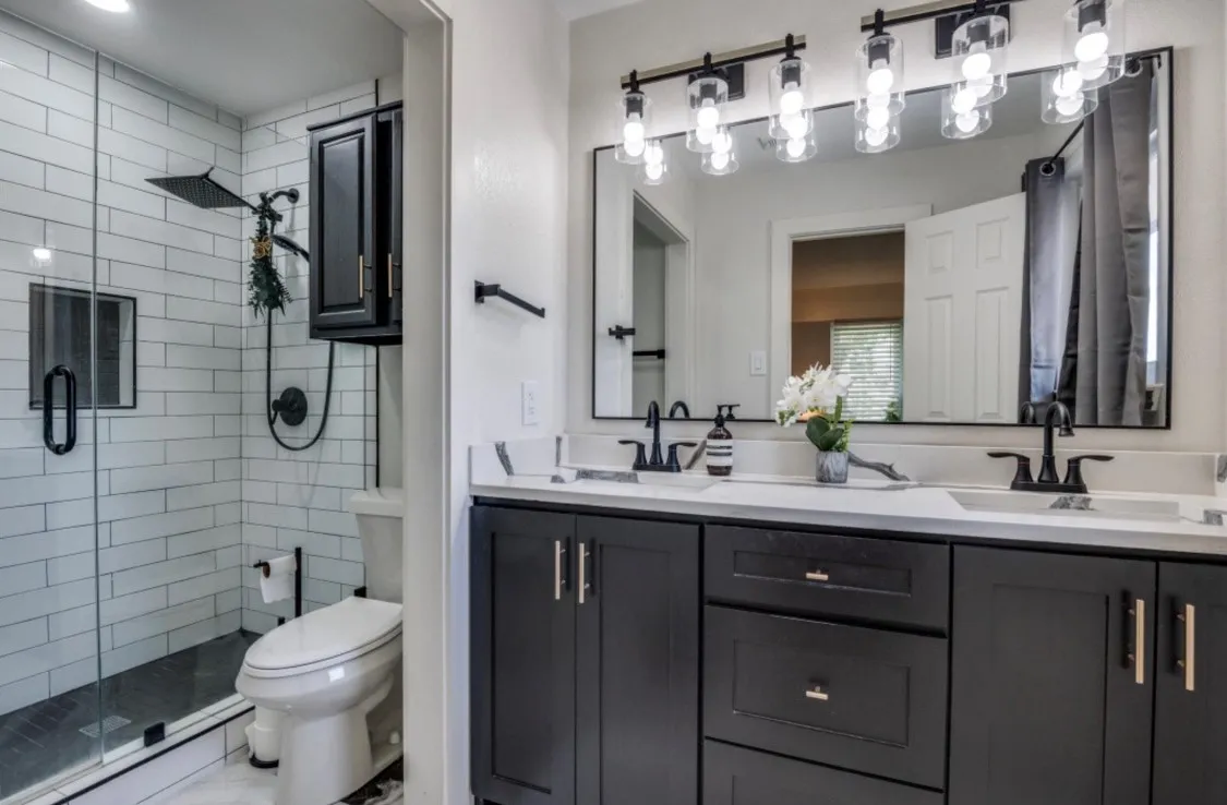 Primary bathroom featuring a double-sink vanity, dark cabinetry, and glass-enclosed shower.