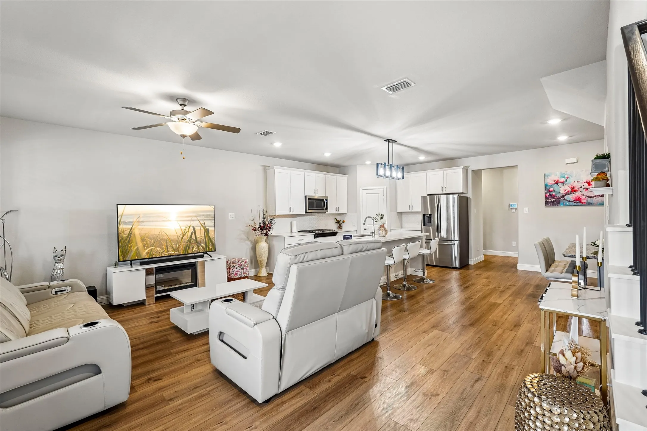 Open-concept living area with wood-finish flooring, recessed lighting, ceiling fan, and white cabinetry
