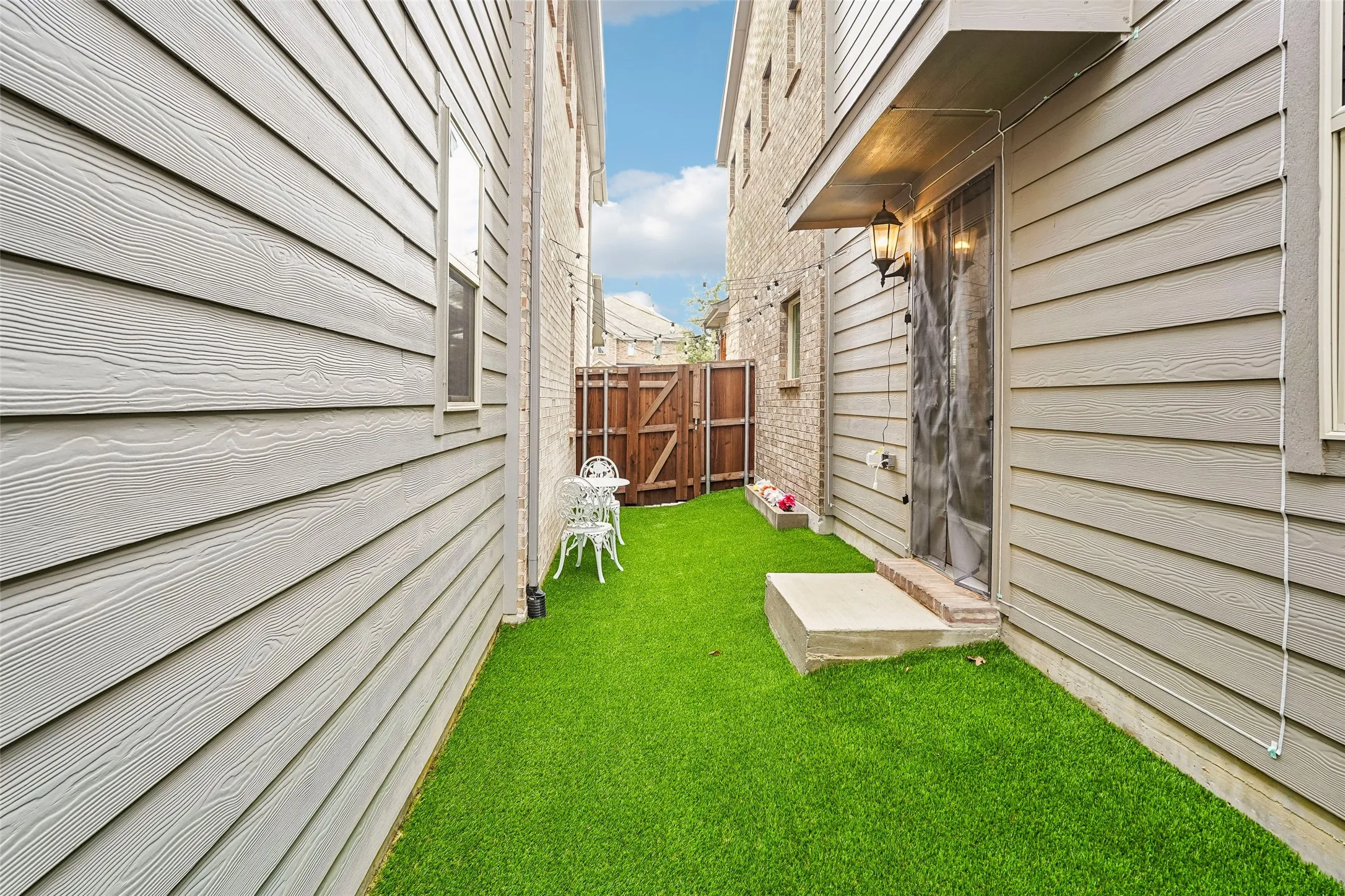 Fenced outdoor area with artificial turf, brick siding, and wood-finish siding