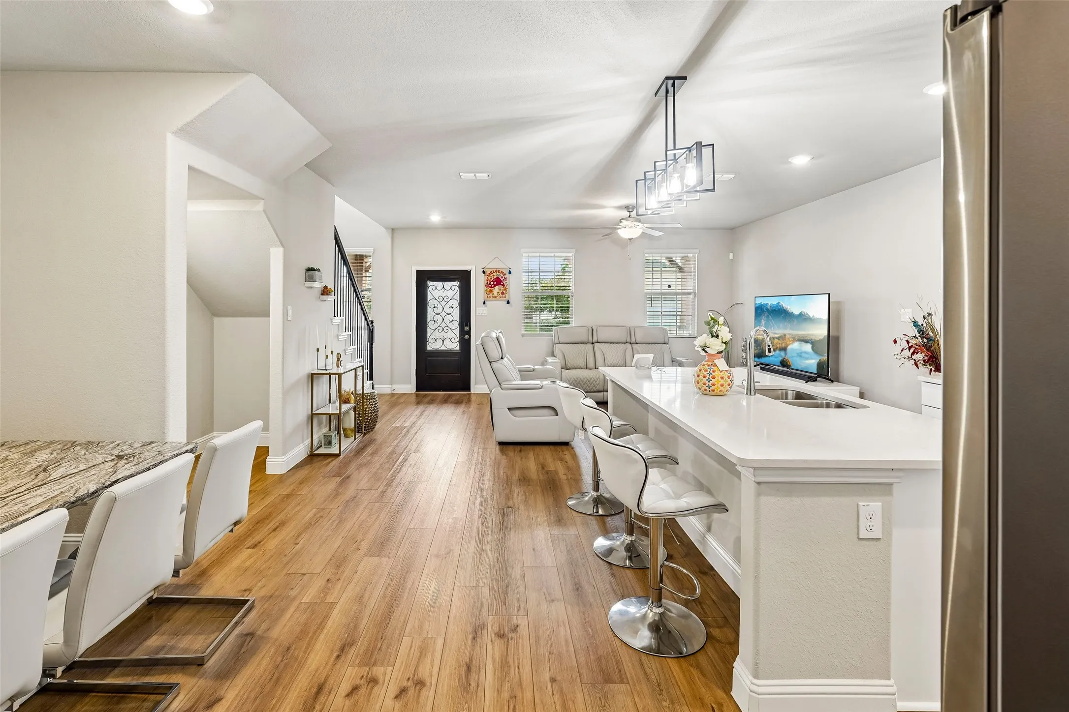 Expansive wood-finish flooring throughout, complemented by a large kitchen island with white countertop and integrated sink
