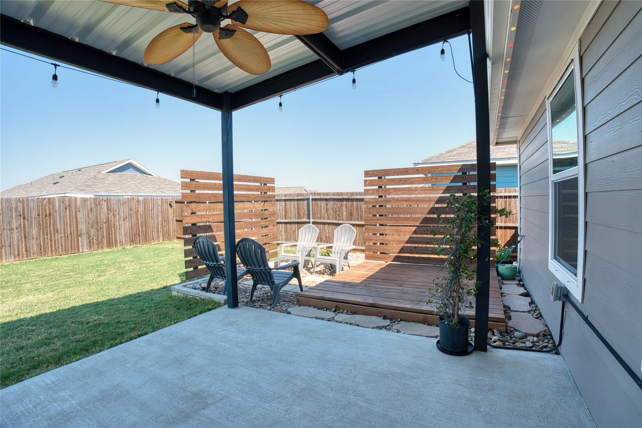 Expansive concrete patio with a covered outdoor living area, featuring a ceiling fan and string lighting