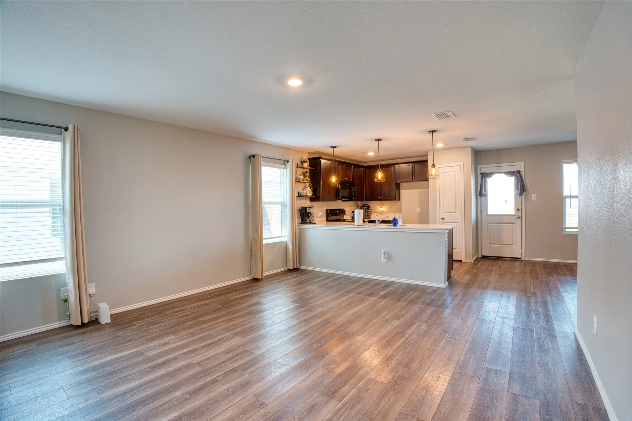 Open-concept living area with wood-finish flooring, recessed lighting, and a partial wall separating the kitchen
