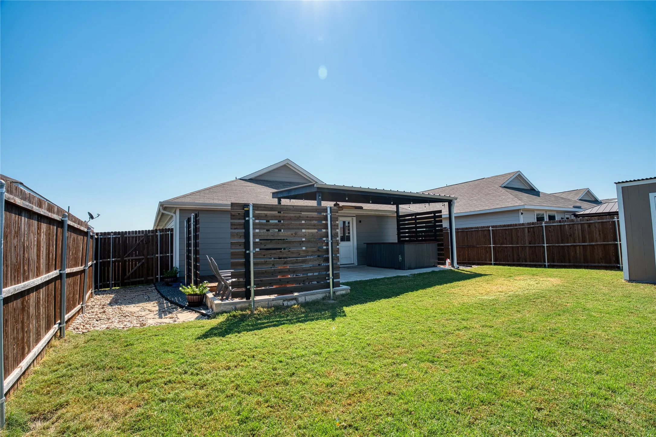 Expansive backyard featuring a covered patio, privacy screen, and a separate storage shed