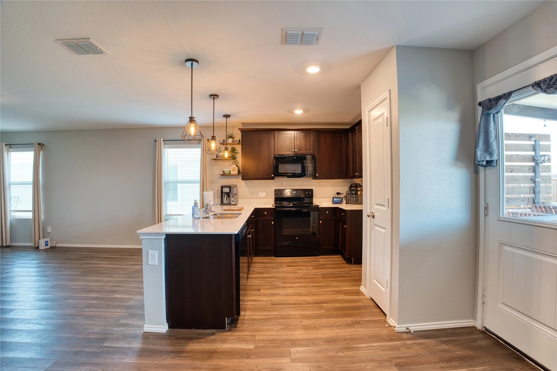 Kitchen featuring dark wood-finish cabinetry, black appliances, white countertops, and three pendant lights over a central island